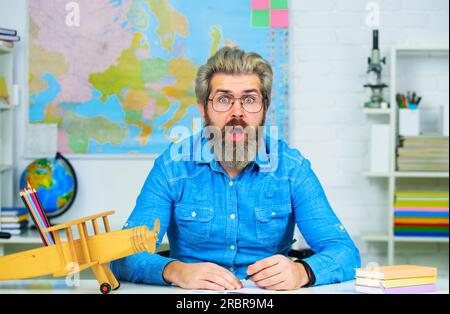 Insegnante barbuto stupito alla scrivania in classe. Studente che si prepara per gli esami universitari. Istruzione. Insegnante maschio barbuto in occhiali alla lezione. Insegnante o. Foto Stock