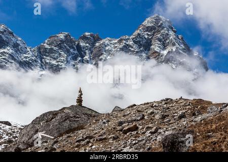 Cairn di montagna sul percorso del campo base dell'Everest in Himalaya, Nepal. Splendido paesaggio nuvoloso con cairn sulla grande roccia e freccia che punta giù per il sentiero Foto Stock