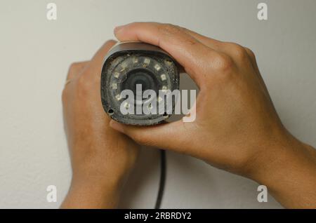 Tecnico qualificato che esegue la manutenzione di una telecamera di sicurezza bianca, rafforzando l'aspetto della protezione e della sorveglianza. Foto Stock