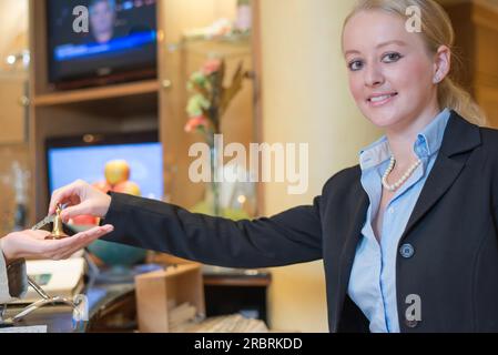 Una giovane e attraente receptionist sorridente nella hall dell'hotel che consegna le chiavi della camera a una donna cliente in un concetto di ospitalità, servizio e turismo Foto Stock