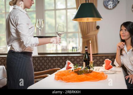 Cameriera donna che serve vino in bicchieri eleganti in un ristorante a una giovane donna attraente seduta a un tavolo formale Foto Stock
