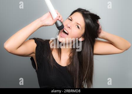 Giovane donna emotiva che canta il suo cuore in un microfono mentre fornisce la voce durante una performance musicale, karaoke o mimare per conto proprio Foto Stock