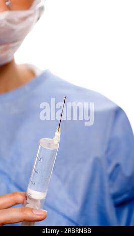 Primo piano delle mani di un medico donna che indossa un abito medico blu e maschera protettiva e occhiali mentre rimuove l'aria da una siringa riempita Foto Stock