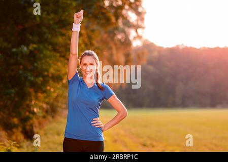 Giubilanti giovane donna fustellatura dell'aria con il suo pugno chiuso come la celebra un successo permanente, mentre in verde e lussureggiante campagna in Early Morning Light Foto Stock