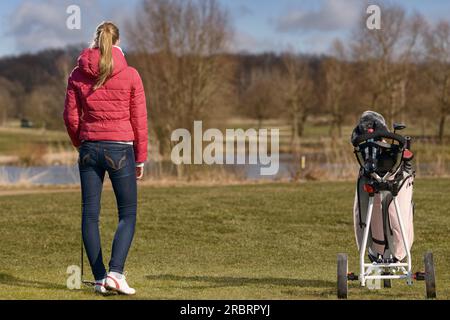 Giovane donna giocando a golf camminare indietro al suo carrello da golf e club attraverso il fairway, vista da dietro Foto Stock