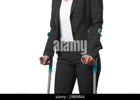 Donna d'affari disabile in Black and White Business Suit che cammina con due stampelle, isolata su sfondo bianco Foto Stock