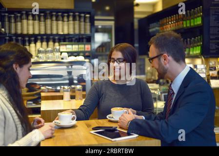 Sorridente cameriera che serve caffè e due giovani donne seduti a un tavolo in un bar o ristorante Foto Stock