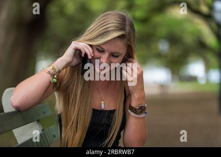 Un modello adolescente biondo parla su un telefono cellulare in un ambiente esterno Foto Stock
