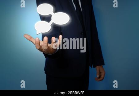 Concetto di comunicazione e dialogo. Uomo d'affari con illustrazione di bolle vocali su sfondo azzurro, primo piano Foto Stock