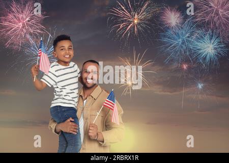 4 luglio - giorno dell'indipendenza dell'America. Un uomo felice e suo figlio che reggono bandiere nazionali degli Stati Uniti contro il cielo con fuochi d'artificio Foto Stock