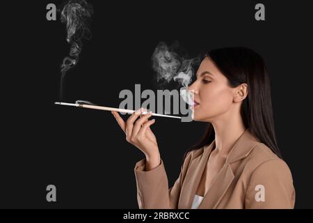 Donna che usa un portabicchieri lungo per fumare su sfondo nero Foto Stock