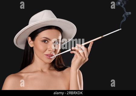 Donna che usa un portabicchieri lungo per fumare su sfondo nero Foto Stock