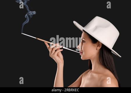 Donna che usa un portabicchieri lungo per fumare su sfondo nero Foto Stock