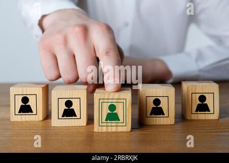 Uomo che mette un cubo di legno con un'icona verde umana davanti agli altri con uno nero al tavolo, primo piano Foto Stock