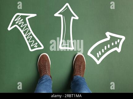 Scegliere una professione futura. Uomo in piedi davanti a cartelli disegnati su sfondo verde, vista dall'alto. Frecce che puntano in direzioni diverse che simboleggiano di Foto Stock