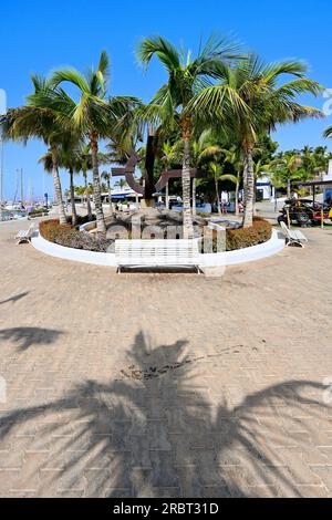 Lanzarote, Isole Canarie, Puerto Calero, ingresso alla principale area dello shopping e dei bar con molte palme di fronte al porticciolo turistico, con un cielo blu intenso Foto Stock