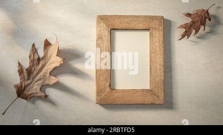 Cornice fotografica vuota e foglie autunnali su sfondo di pietra alla luce del sole Foto Stock