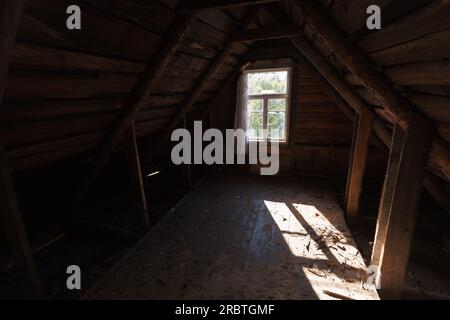 Gli interni in legno sono astratti, con vista prospettica di una sala mansardata abbandonata con la luce del sole che passa attraverso una finestra vuota Foto Stock