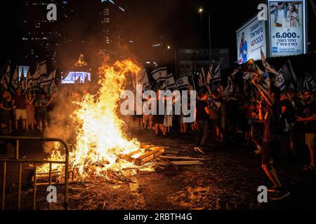 Tel Aviv, Israele. 5 luglio 2023. I manifestanti contro la riforma cantano intorno a un falò sull'autostrada Aayalon bloccata durante la manifestazione. Migliaia di israeliani sono scesi in strada e hanno bloccato l'autostrada Ayalon a Tel Aviv scontrandosi con la polizia che ha usato cannoni ad acqua e ufficiali di polizia a cavallo e arresti per disperdere i manifestanti dopo che il capo della polizia di Tel Aviv Amichai Eshed ha annunciato le sue dimissioni dalla forza. (Immagine di credito: © Matan Golan/SOPA Images via ZUMA Press Wire) SOLO USO EDITORIALE! Non per USO commerciale! Foto Stock