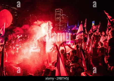 Tel Aviv, Israele. 6 luglio 2023. I manifestanti anti anti-riforma sventolano la bandiera israeliana e tengono un bagliore sull'autostrada bloccata di Ayalon mentre vengono spruzzati da cannoni ad acqua della polizia durante la manifestazione. Migliaia di israeliani sono scesi in strada e hanno bloccato l'autostrada Ayalon a Tel Aviv scontrandosi con la polizia che ha usato cannoni ad acqua e ufficiali di polizia a cavallo e arresti per disperdere i manifestanti dopo che il capo della polizia di Tel Aviv Amichai Eshed ha annunciato le sue dimissioni dalla forza. (Immagine di credito: © Matan Golan/SOPA Images via ZUMA Press Wire) SOLO USO EDITORIALE! Non per USO commerciale! Foto Stock