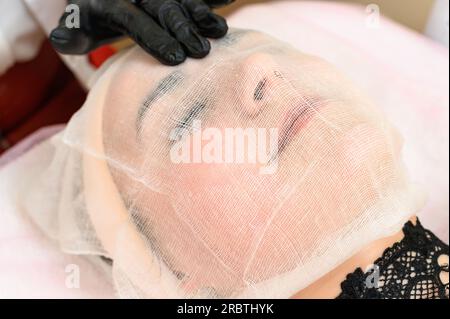 Un estetista mette una garza sul viso del paziente, curando la pelle secca e sensibile. Foto Stock