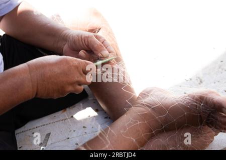 L'uomo sta riparando una rete da pesca su una barca in un villaggio, Indonesia Foto Stock