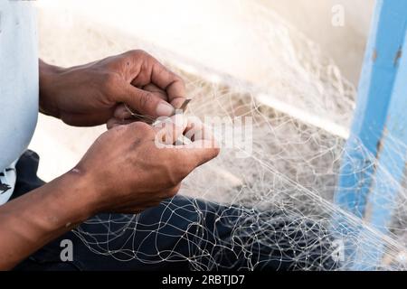 L'uomo sta riparando una rete da pesca su una barca in un villaggio, Indonesia Foto Stock