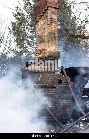 Resti di una casa dopo un incendio. Il tubo in mattoni della stufa è protetto da fumo denso. Una vista verticale della cenere cupa Foto Stock