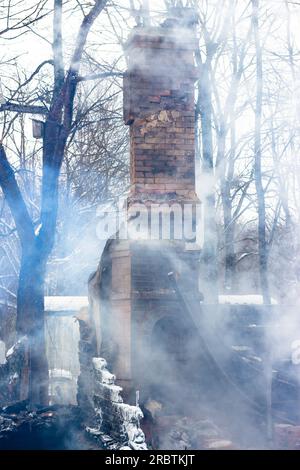 Resti di una casa dopo un incendio. Il tubo in mattoni della stufa è protetto da fumo denso. Una vista verticale della cenere cupa Foto Stock