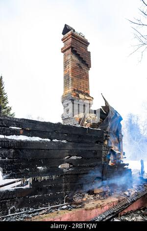 Resti di una casa dopo un incendio. Il tubo in mattoni della stufa è protetto da fumo denso. Una vista verticale della cenere cupa Foto Stock