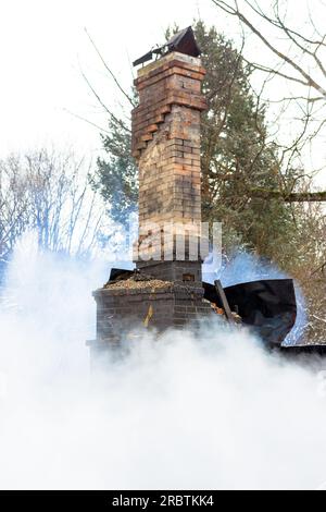 Resti di una casa dopo un incendio. Il tubo in mattoni della stufa è protetto da fumo denso. Una vista verticale della cenere cupa Foto Stock