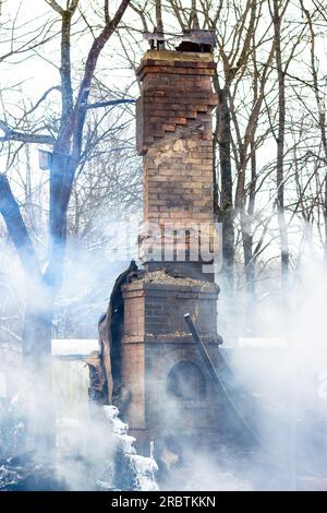 Resti di una casa dopo un incendio. Il tubo in mattoni della stufa è protetto da fumo denso. Una vista verticale della cenere cupa Foto Stock