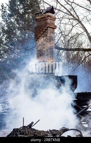 Resti di una casa dopo un incendio. Il tubo in mattoni della stufa è protetto da fumo denso. Una vista verticale della cenere cupa Foto Stock
