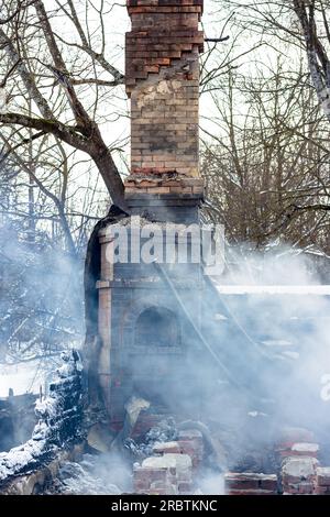 Resti di una casa dopo un incendio. Il tubo in mattoni della stufa è protetto da fumo denso. Una vista verticale della cenere cupa Foto Stock
