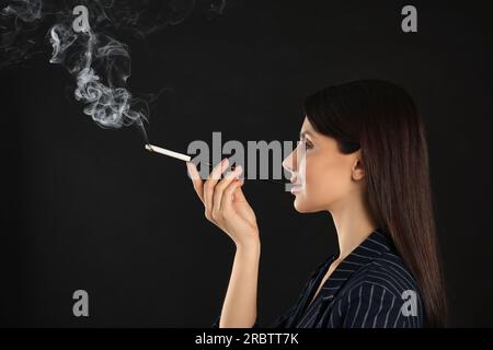 Donna che usa un portabicchieri lungo per fumare su sfondo nero Foto Stock