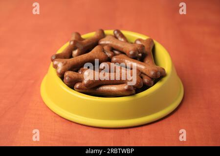 Ciotola gialla con biscotti di cane a forma di osso su un tavolo di legno, primo piano Foto Stock