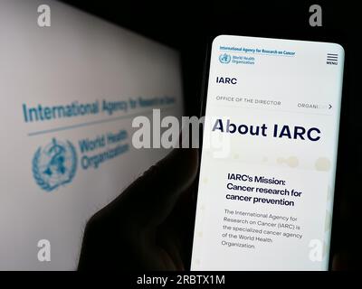 Persona che detiene il cellulare con pagina web dell'Agenzia internazionale per la ricerca sul cancro (IARC) sullo schermo con logo. Concentrarsi sul centro del display del telefono. Foto Stock