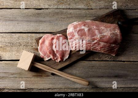 Cottura dello schnitzel. Carne di maiale cruda e tenderizer su tavolo in legno, vista dall'alto Foto Stock