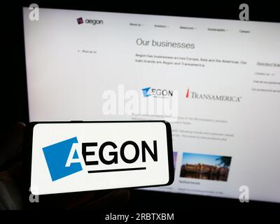 Persona che possiede uno smartphone con il logo della società olandese di servizi finanziari Aegon N.V. sullo schermo di fronte al sito web. Concentrarsi sul display del telefono. Foto Stock