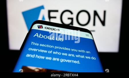 Smartphone con sito Web della società olandese di servizi finanziari Aegon NV sullo schermo davanti al logo aziendale. Mettere a fuoco in alto a sinistra sul display del telefono. Foto Stock