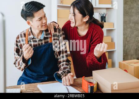 Una giovane coppia asiatica mostra gioia e sorrisi quando vede il volume delle vendite e gli ordini dei clienti superare le aspettative. pmi o piccole Foto Stock