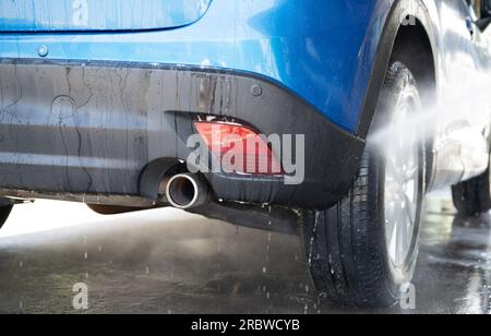 Lavaggio auto con spruzzo d'acqua ad alta pressione. Pulizia dell'auto. Concetto di servizio Auto Care. Pulizia del veicolo. Spruzzo di acqua ad alta pressione sulla ruota della vettura Foto Stock