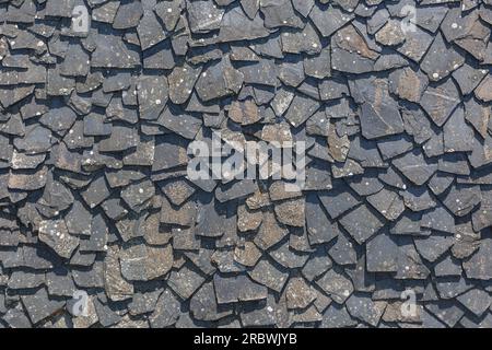 Vista dettagliata della struttura della parete rivestita in modo casuale con pannelli in ardesia, materiale tipico e tradizionale in pietra di scisto, utilizzato come rivestimento impermeabile esterno Foto Stock