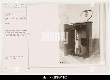 '6 FEBBRAIO 1919: Il soldato Tyrell si trova accanto a un telefono con allarme antincendio montato su un palo. La porta del telefono è aperta e mostra una luce rossa sopra di essa. Il palo si trova all'angolo nord-ovest dell'edificio n. 95. Questa fotografia è stata approvata dal M.I.D. censor il 17 febbraio 1919." Foto Stock