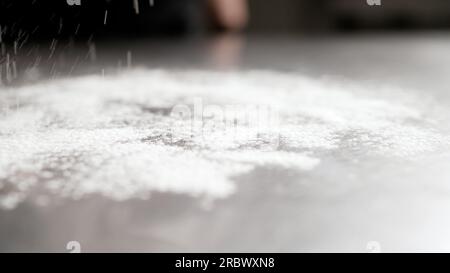 Cospargere di farina su sfondo nero. Primo piano della mano di una giovane casalinga che spruzza farina sul tavolo. Il cuoco prepara la farina da cuocere su Foto Stock