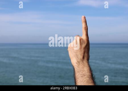 Fare la mano, mostrando il simbolo del gesto numero uno su sfondo blu estate cielo natura. Numero di gesture 1. Numero uno nella lingua dei segni. Foto Stock