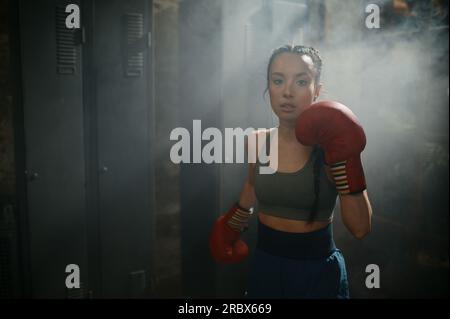 Ritratto di una donna pugile stanca e sudata in fumo guardando la fotocamera Foto Stock