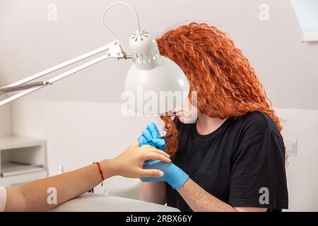 Trattamento manicure di un giovane lavoratore dai capelli rossi nel salone manicure e pedicure. Foto Stock