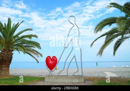 Impressionante scultura moderna dell'uomo con un cuore rosso sulla spiaggia del mare nero della città di Batumi, Georgia Foto Stock
