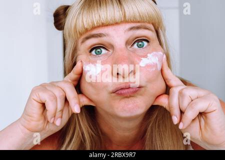 Ritratto attraente donna bionda di mezza età con crema cosmetica Foto Stock